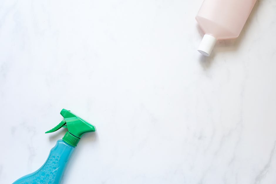 Flat lay of cleaning spray and bottle on a white surface with ample copy space.